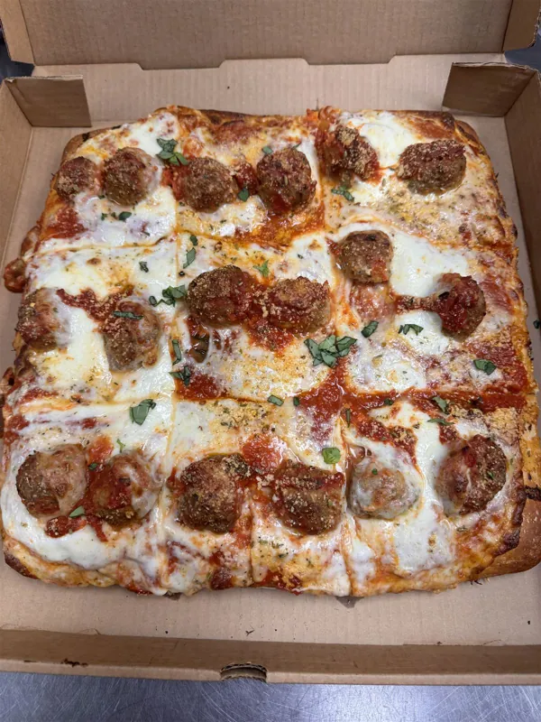 Square Sicilian pie with homemade meatballs, mozzarella, red sauce and basil in a takeout box