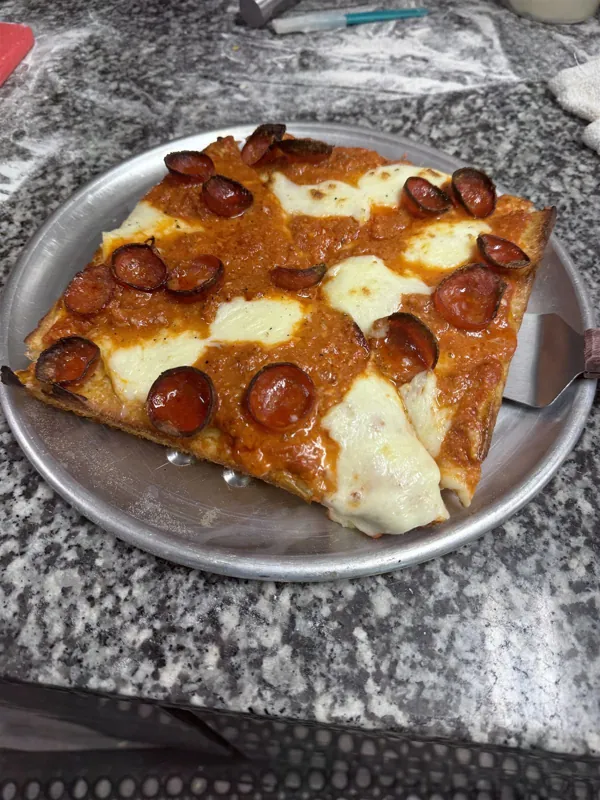 Thick square Sicilian slice with cup pepperoni, sauce on top and pools of mozzarella on a round metal tray